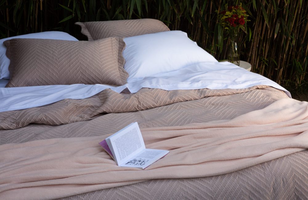 Imagem de uma cama arrumada com colchas em textura geométrica.