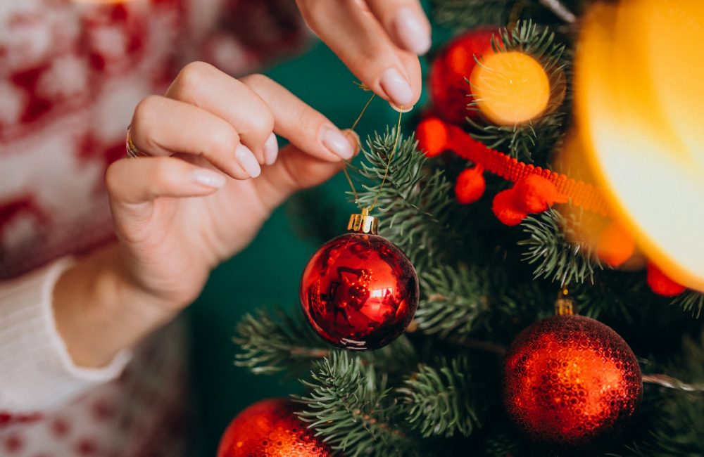 Female hands close up, decorating christmas tree with red toys